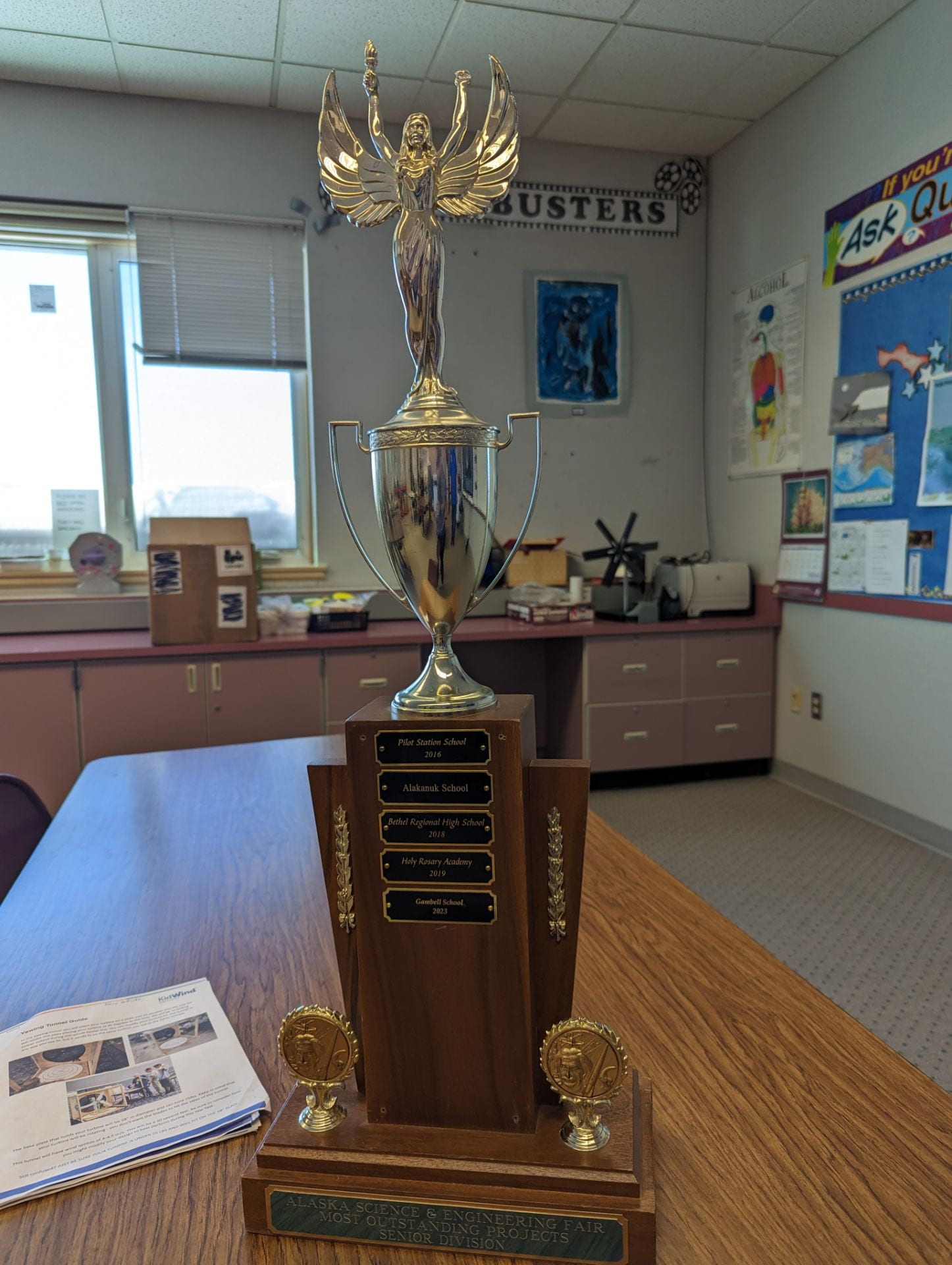 A large trophy topped with a winged figure sitting on a classroom desk.